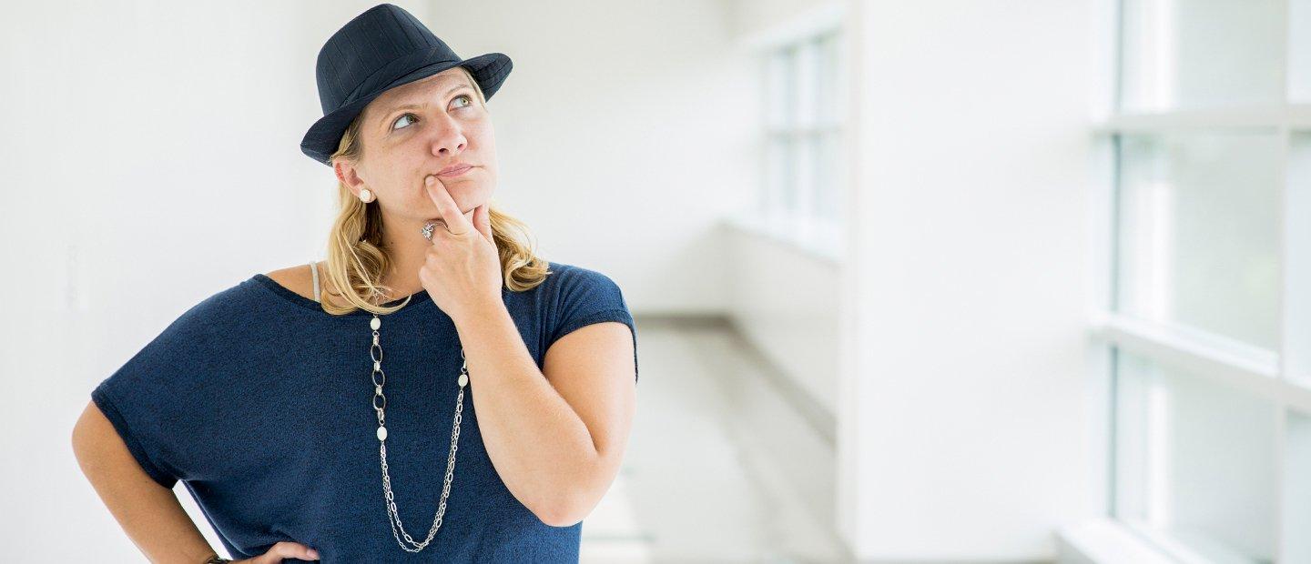 woman in a blue shirt and hat with her hand on her chin and an inquisitive look on her face