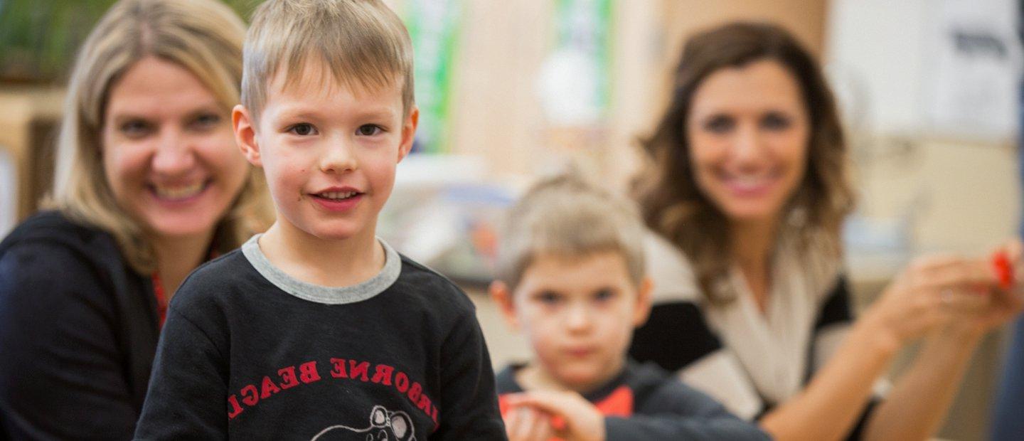 kid looking at the camera with two women and one other kid in the background